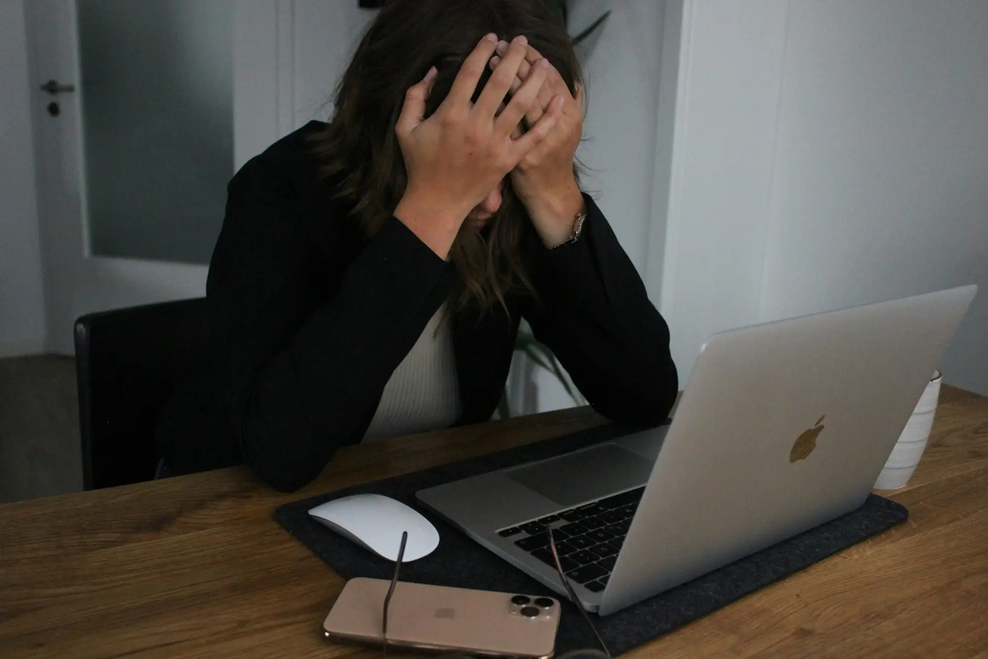 Woman sitting at laptop with head in her heads, appearing overwhelmed. Hiring a fashion or beauty PR agency